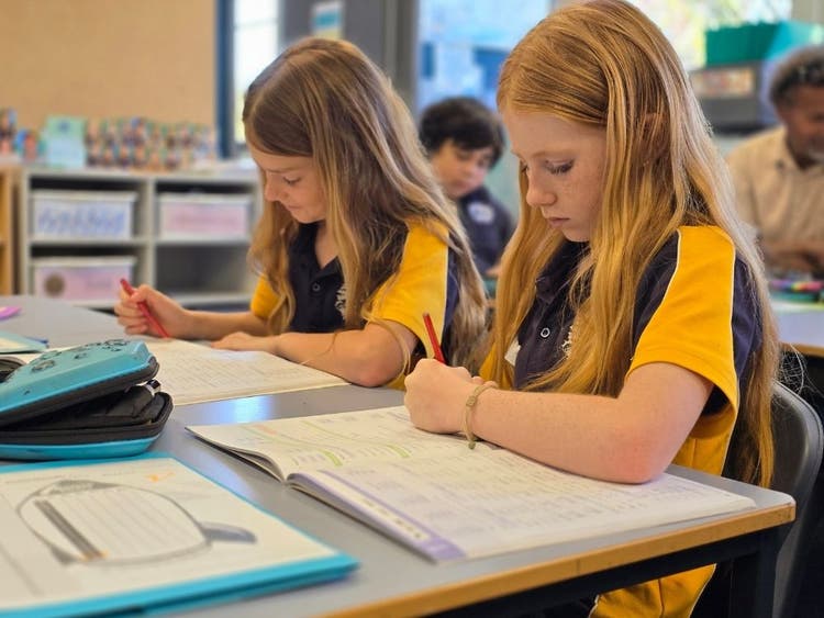 Photo of two students working at their desks in their classroom.