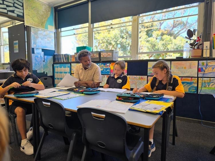 Photo of students working with an SLSO at their desk in a classroom.