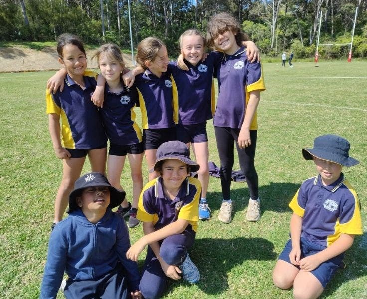 Photo of a group of students at a sporting event, in school uniform and hats. All students have big smiles
