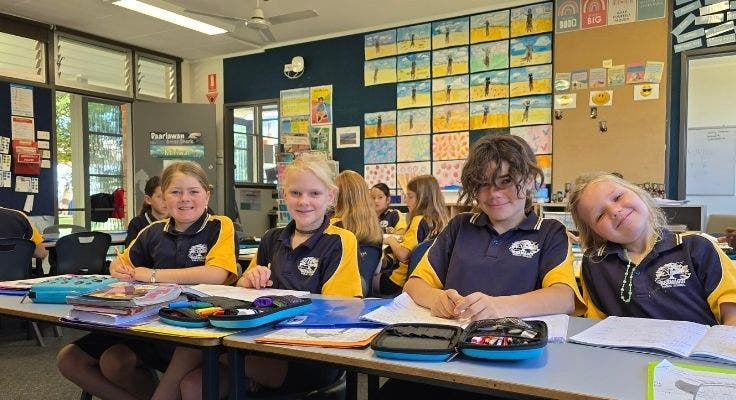 Students in classroom smiling for photo. Students are working in their workbooks.