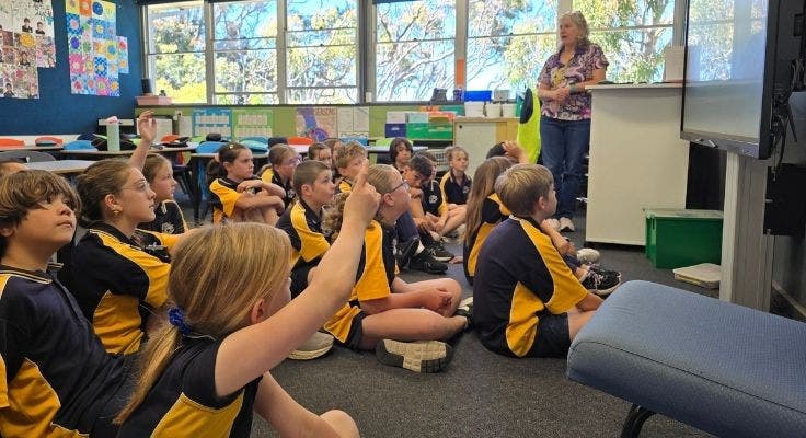 Students sitting on the floor in their classroom with teacher at front of class.